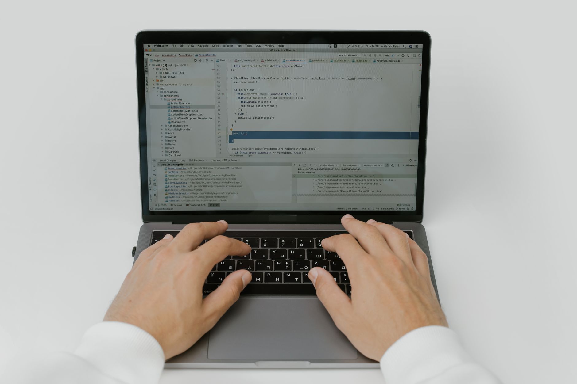 A close-up of two hands typing on a laptop keyboard, the screen above them filled with code.